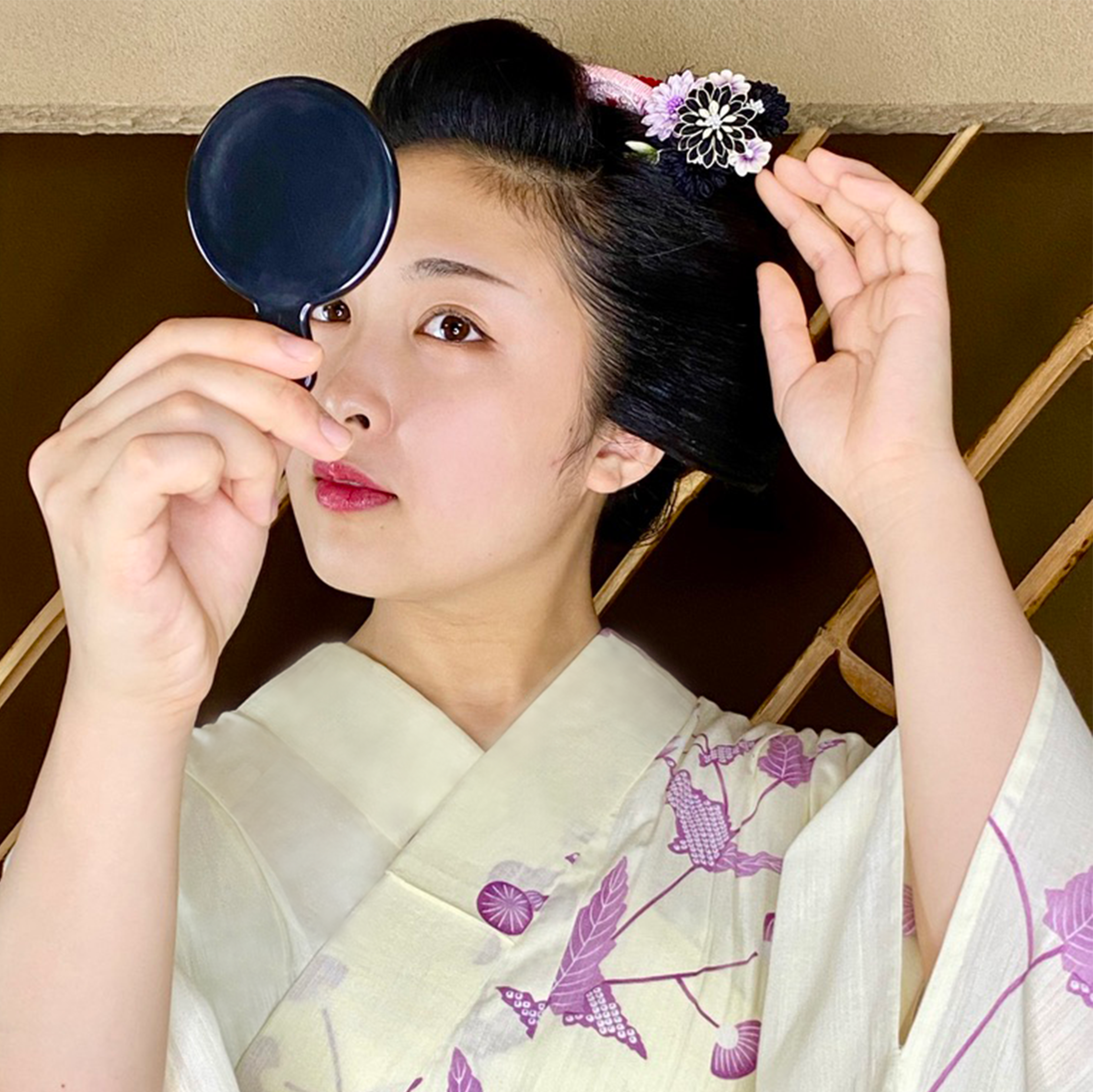 舞妓さんが手鏡でかんざしを確認している